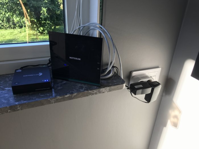 Dayton Audio förstärkare och Netgear-enhet med trassel av kablar på en fönsterbräda.