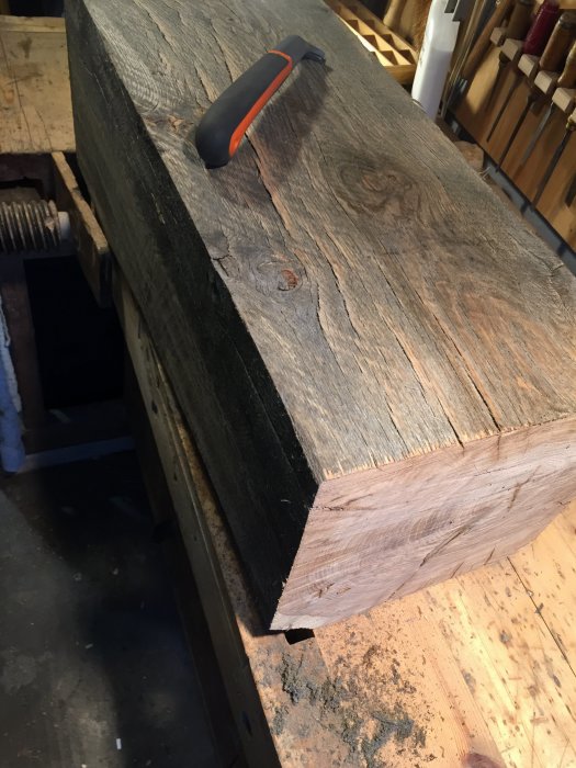 Grov träplanka med smuts och möjliga hyvlingsmärken på ett arbetsbord med en skrapa ovanpå.