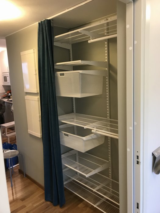 Välfylld vit garderob med flera öppna hyllplan och utdragbara korgar, precist installerade i ett rum.
