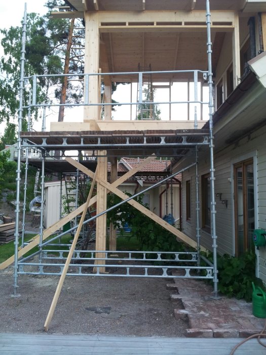 Byggställning framför hus under renovering med träpelare och bjälkar synliga.