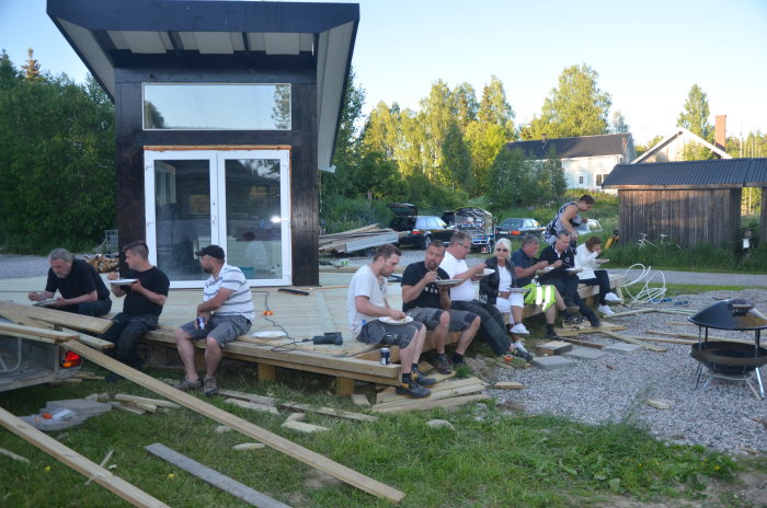 Grupp personer tar en paus från byggandet av trall, äter tillsammans vid konstruktionen.