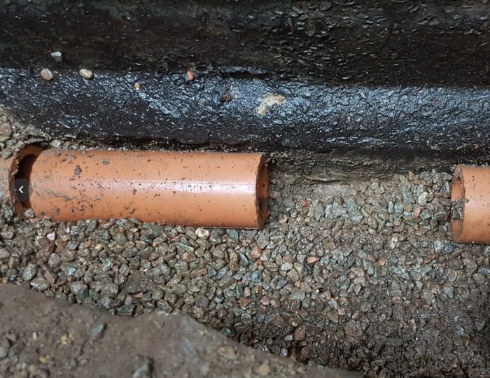 Tegelrör omgivet av grus och kall asfalt på väggen som ser blött ut efter att ha spolats av.