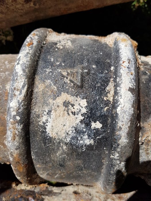 Närbild på en gammal sliten maskindel med möjliga tillverkarmärkningar täckta av smuts och rost.