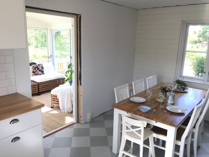 Nyrenoverat vitt kök med träbänkskivor, ett matbord klart för middag och utsikt till en uteplats.