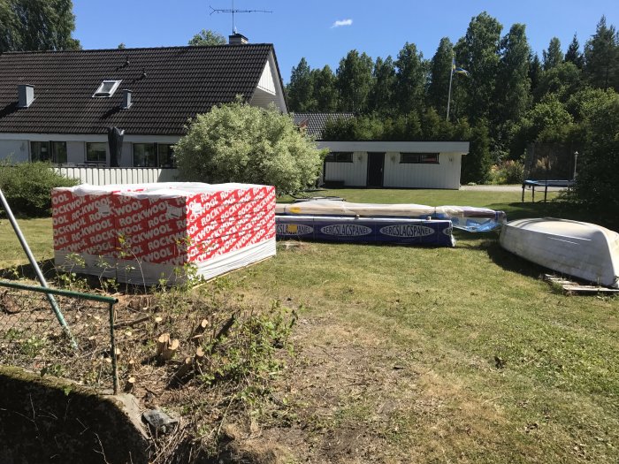 Nyinköpt byggmaterial och två båtar på en gräsmatta framför ett hus.