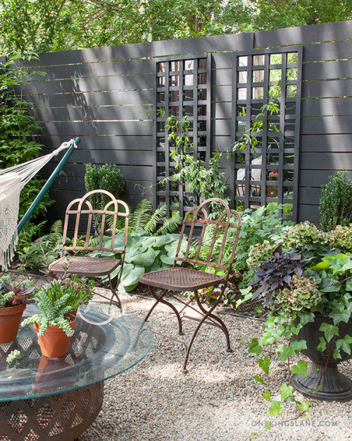Trädgård med dekorativt svart plank med reglerbart genomsläpp, metallstolar och gröna växter.