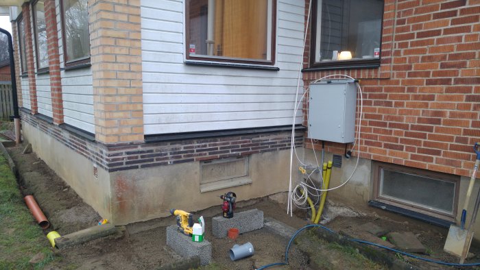 Exteriör vägg under renovering med elektrisk utrustning, verktyg och öppen grävning.