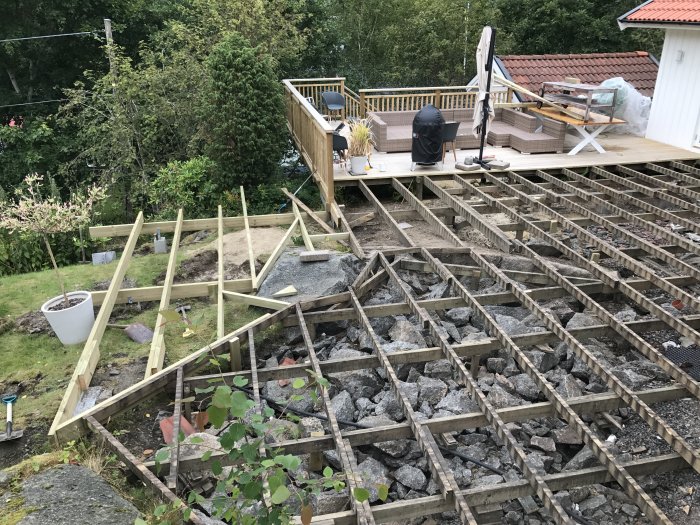 Nybyggda träreglar för en altan under konstruktion med befintlig stabiliserad del i bakgrunden.