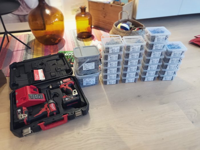 Nya skruvdragare i ett etui och många lådor med skruvar på trägolv.