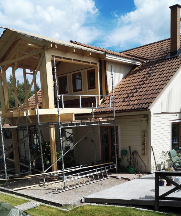 Pågående bygge av en trästrukturell tillbyggnad på ett hus, med ställningar och en planerad balkongplats markerad med röd ram.