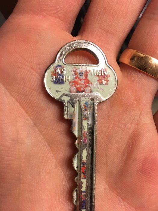 Nyckel med texten "AS 37HH Italy" hålls i en hand, nyckelns tänder och slitage synliga.