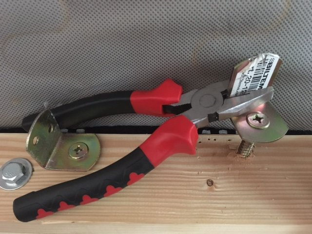 Ett staketbeslag fäst i trä med en tång på, nära en hammare och skiftnyckel, verktyg för hemmafix.