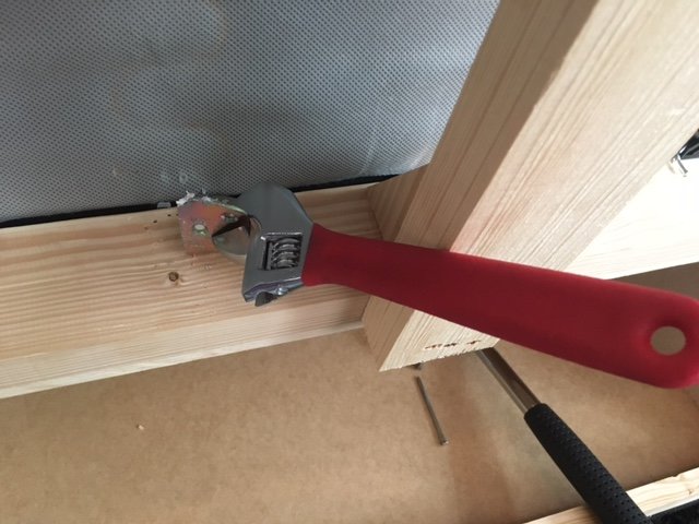 Användning av skiftnyckel för att skruva fast staketbeslag i träkonstruktion.