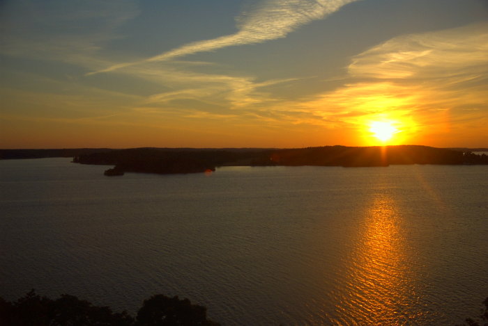 Solnedgång över vatten med reflexion och silhuett av träd mot Färingsö från Gåseborg, Järfälla 2002.