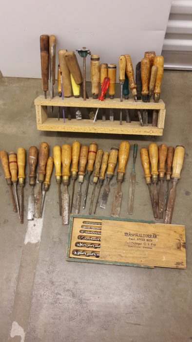 Gamla trähyvlar och stämjärn i olika storlekar och skick på en arbetsbänk med en låda märkt 'Träspiralborrar'.
