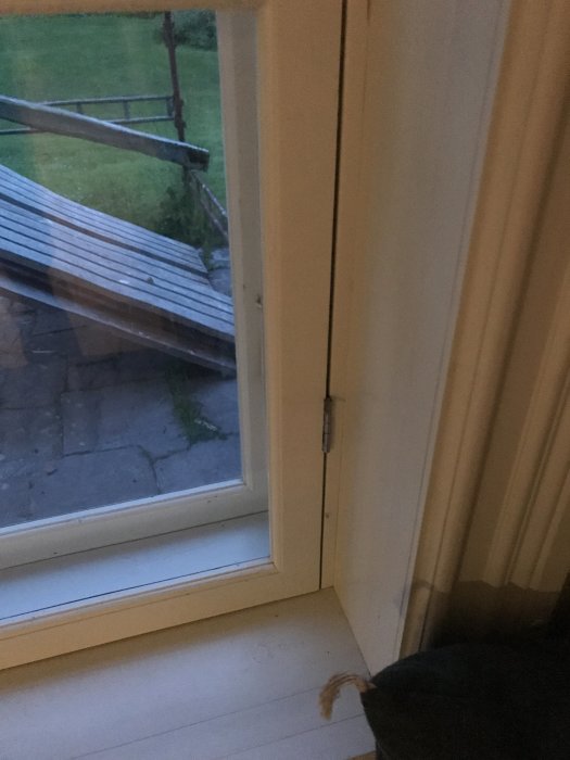 Gångjärn med uttagen sprint på en vit fönsterkarm, utomhusvy synlig genom fönstret.