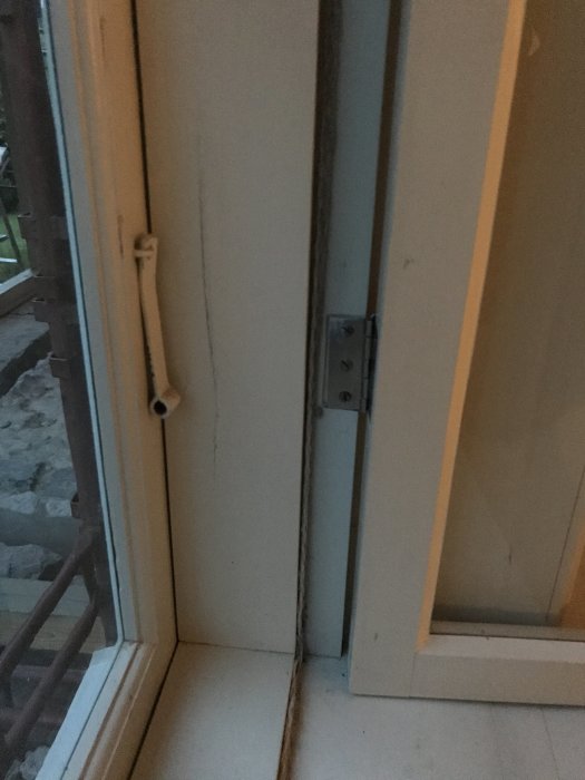 Fönstergångjärn på vitmålad träkarm med en synlig lös sprint och öppen fönsterlucka.