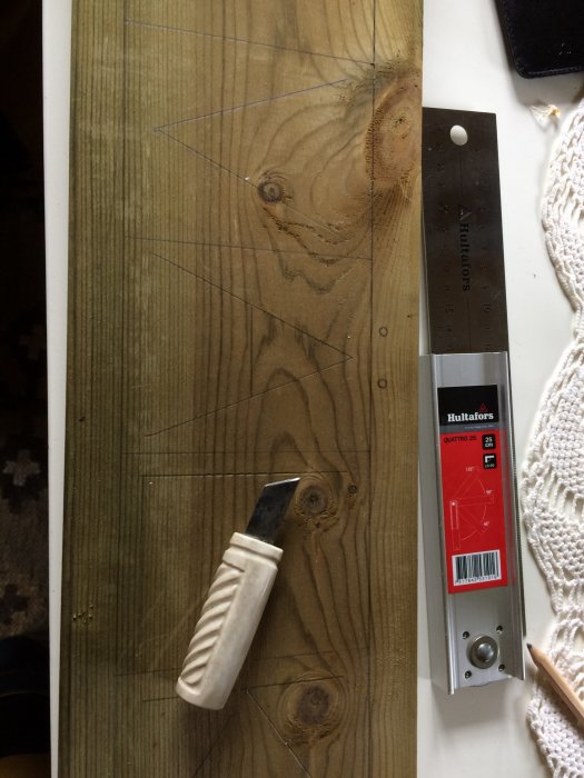 Gravyrkniv och tumstock på träplanka med uppritade linjer för byggprojekt.