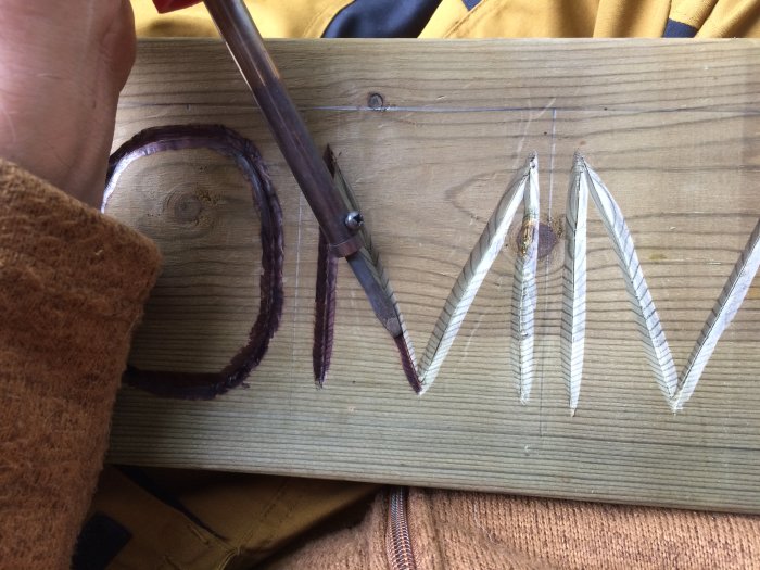 Hand bränner in text med lödkolv i träplanka.