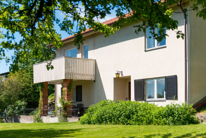 Ett hus med trädgård, putsad fasad och fönster med bruna persienner.