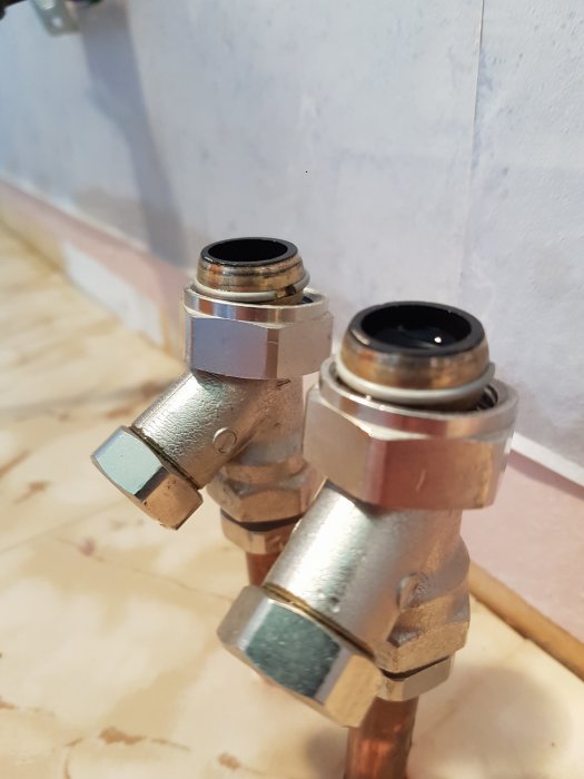 Två kopparvattenrör med vinkelkopplingar mot en kaklad vägg.