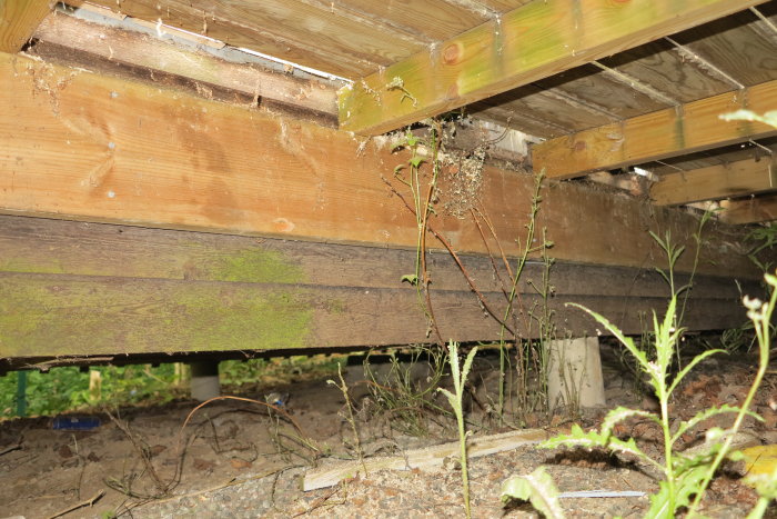 Infästning av trädäck mot husvägg med synlig skräpansamling och fuktspår.