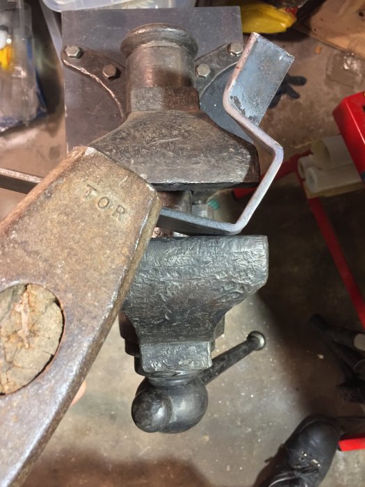 Närbild på ett använd skruvstäd med märkningen 'TOR', monterat på ett arbetsbänkshörn i en verkstad.