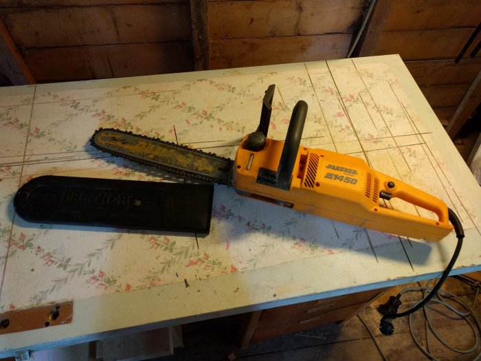 Partner 1450 elmotorsåg med skyddsöverdrag som ligger på ett blommigt arbetsbord.