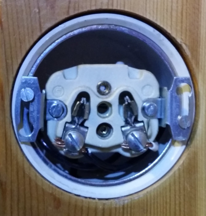 Öppet äldre elektriskt uttag i en panel med tre osäkra kopplingar och ingen märkbar spänning.