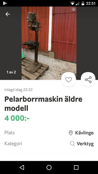 Äldre pelarborrmaskin modell på pall framför röd ladugårdsdörr, möjlig renoveringsprojekt.