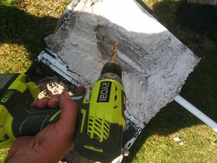 En person som håller i en grön och svart borr för att borra i en betongplatta utomhus.