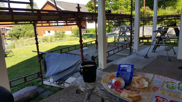 Frukost på en pågående verandabygge med kaffekopp, smörgåsar och byggmaterial i bakgrunden.