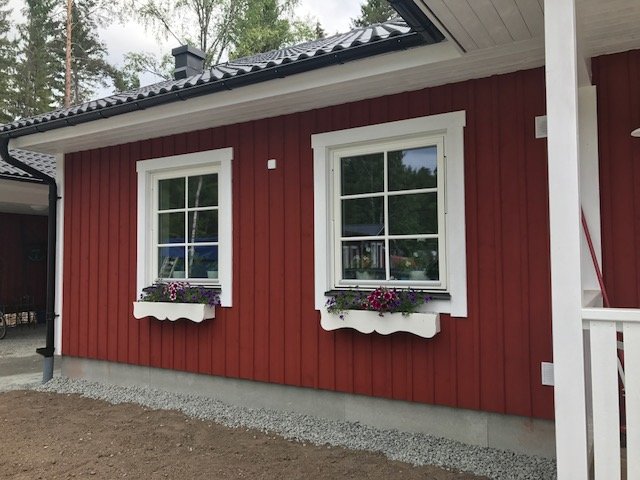 Rött hus med vita fönster och specialtillverkade blomlådor, grusad gång och furstukvist.