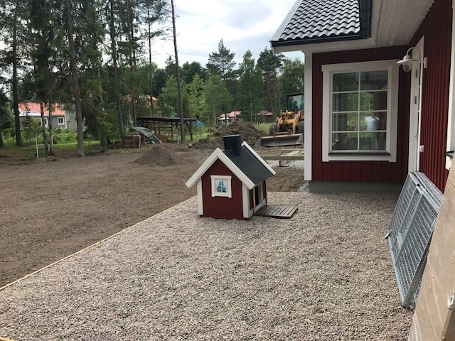 Nybyggt hundhus med ramp vid grusad gård med nivellerad jord och påbörjad altanbyggnad i bakgrunden.