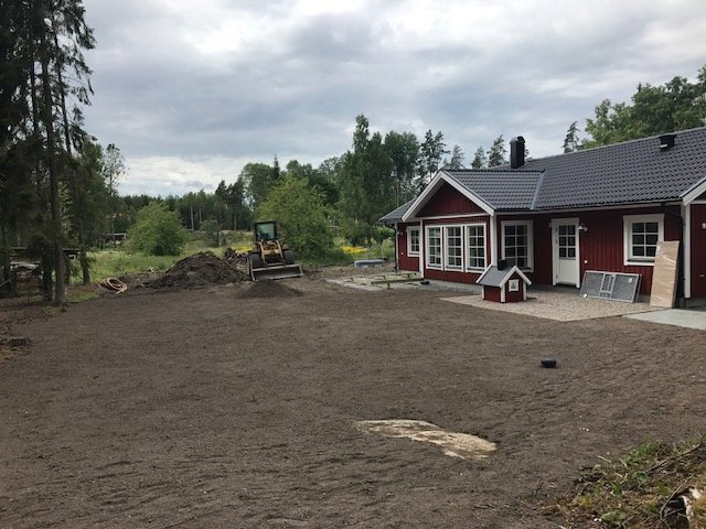 Röd villa med vit inramning, nyjämnad tomt med pågående arbete och mindre byggnader för hundar.