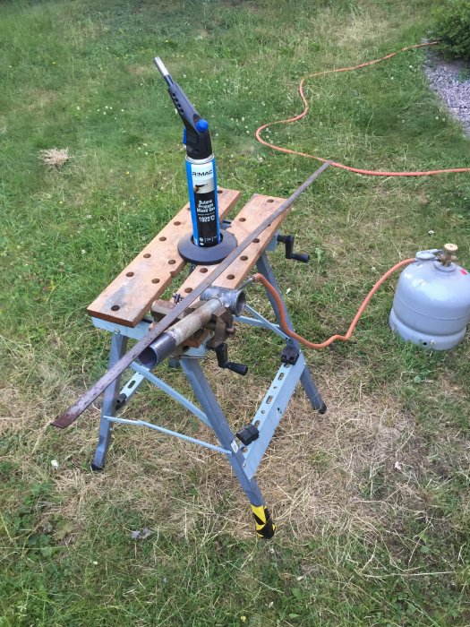 Brännare monterad på arbetsbänk med järn- och kopparrör kopplat till gasolflaska på gräs.