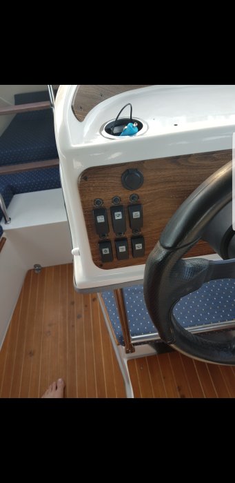 Panel med sex brytare och en halvt intryckt pinne ombord på en båt, nära ratten.
