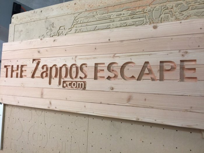 Utskurna träbokstäver med texten "THE ZAPPOS ESCAPE .com" på en plywoodvägg som exempel på notfräs resultat.