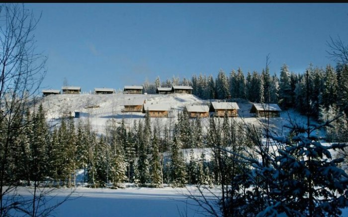 Stugby vintertid med stugor som står på stenar i snötäckt landskap, utan synligt berg i bakgrunden.