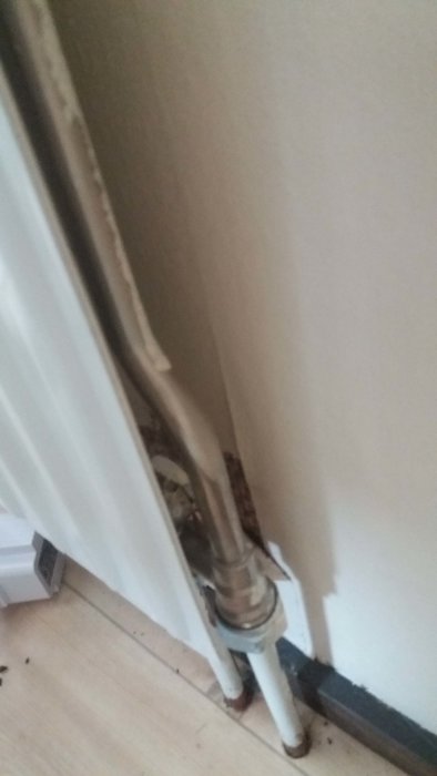 Rörkopplingar till radiator med synliga ventiler och anslutningar mot vit vägg och golv.