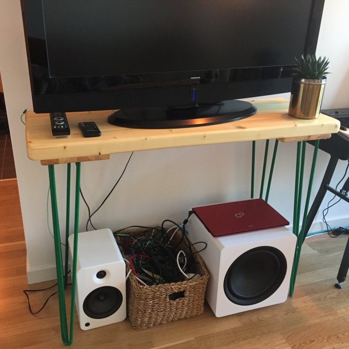 Hemmagjort bord används som TV-bänk med gröna ben, TV, högtalare, och korg med kablar.