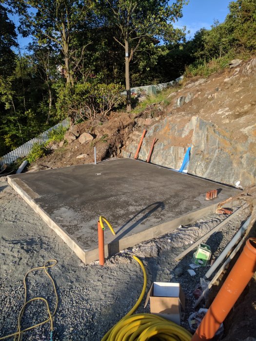 Nygrundad garageplatta som torkar, omringad av makadam och byggmaterial, utomhus i dagsljus.