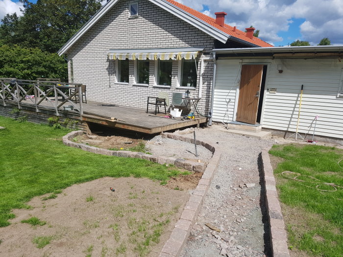 Vit tegelhus med en veranda och en utgrävd gångväg kantad med stenar där den gamla trappan varit.