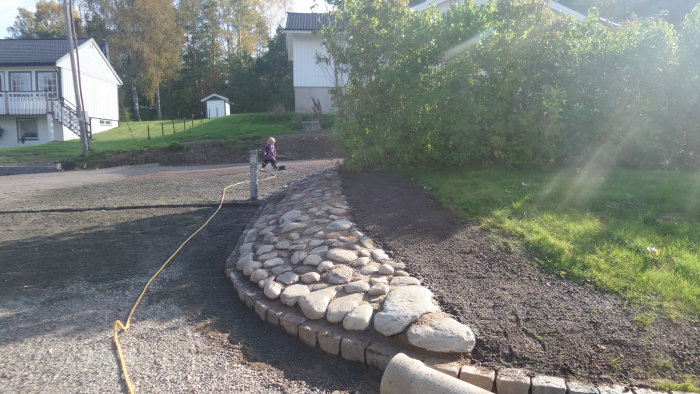 Ny anlagd rabattkant av runda stenar där en gammal trappa tidigare varit, med hus och trädgård i bakgrunden.