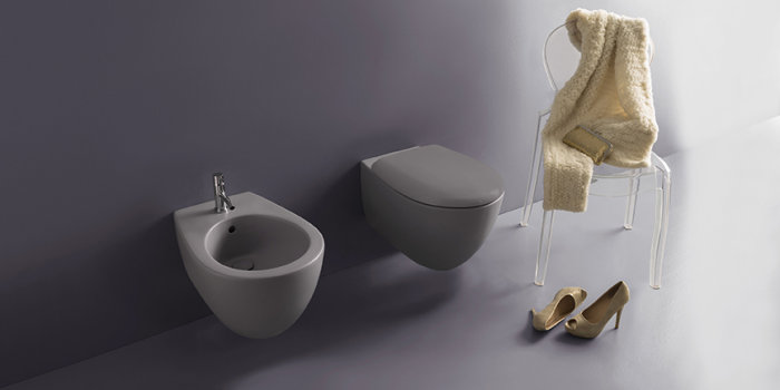 Väggmonterad toalett och bidé i minimalistisk design med en stol och ett par skor i ett stilrent badrum.