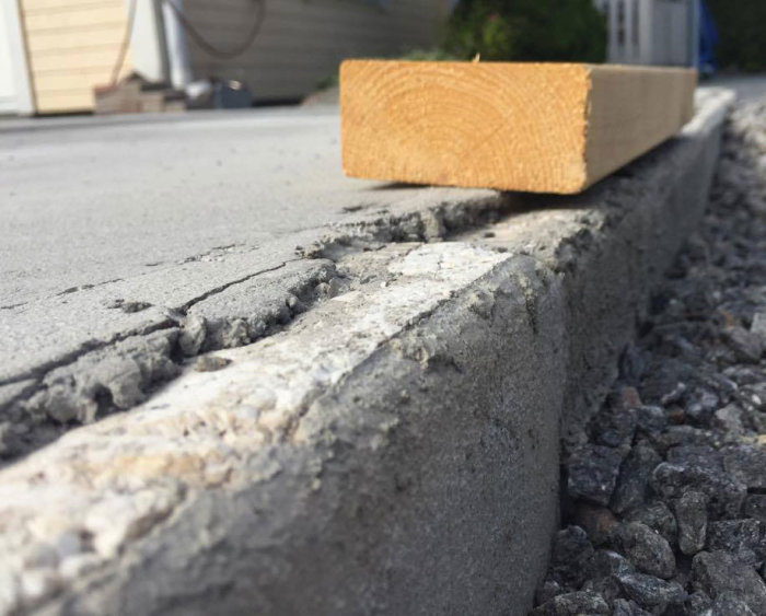 Ojämn husgrunds betongplatta som sticker ut över kantelementet med en träbit som referens.