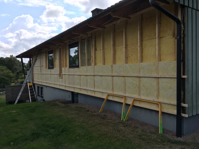 Isolerad husfasad under renovering med stege och skyddsräcken.