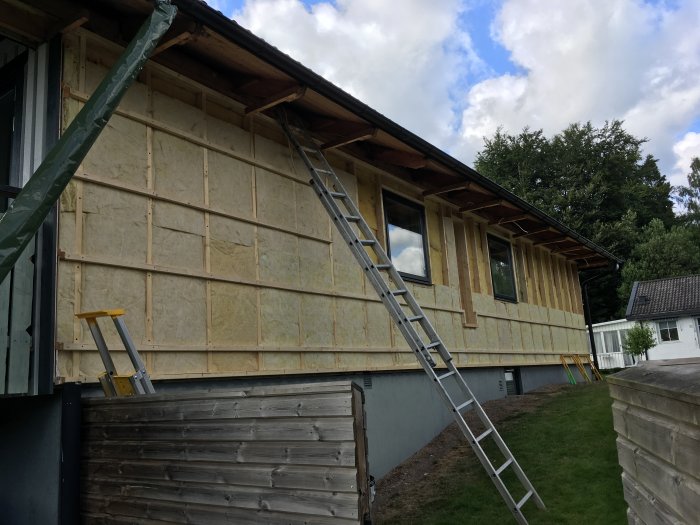 Hus under renovering med ny isolering och trästomme, stege lutad mot byggnaden.