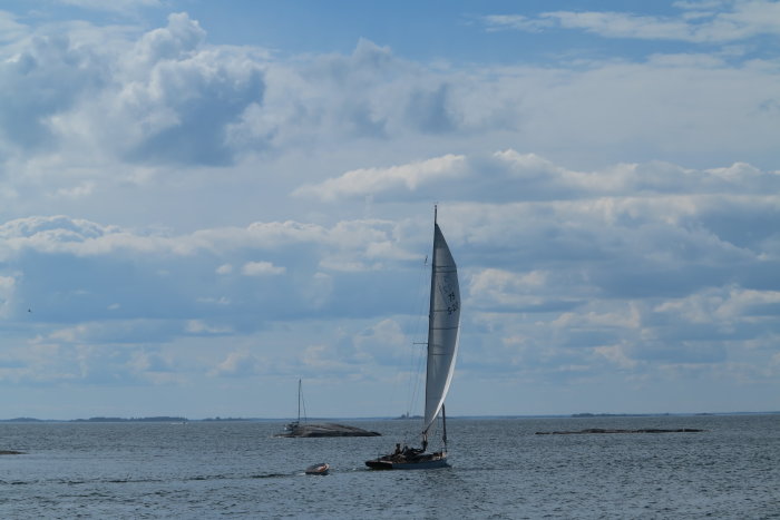 Segelbåtar på vattnet, framför ett landskap med himmel och moln, gammal mätregel Q75.