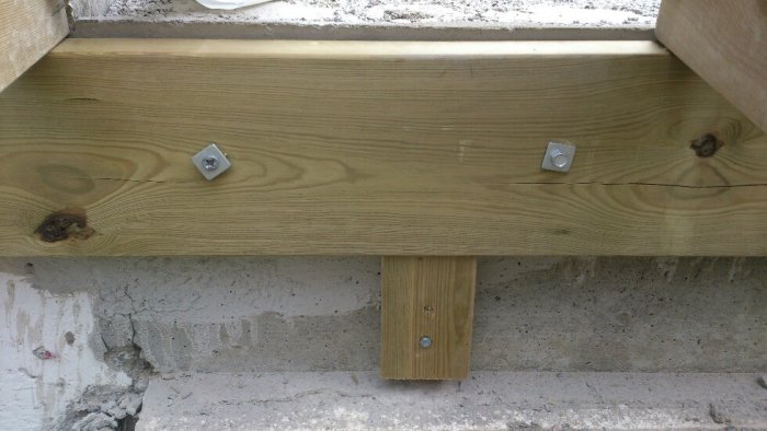 Träbjälke fäst vid betong med nya sexkantshuvudskruvar och plugg samt en gammal kryssspårsskruv.